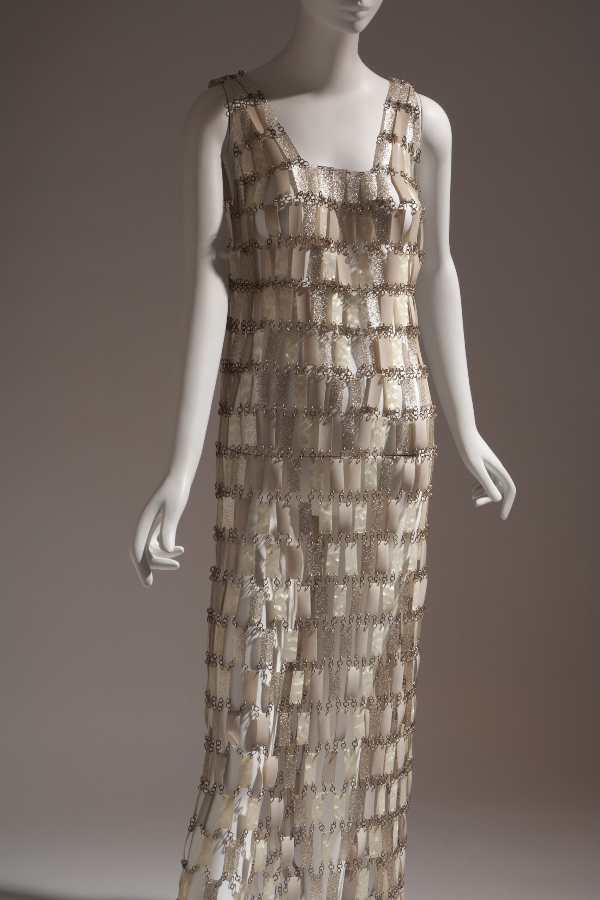 Ankle-length, sleeveless, shift-silhouette wedding dress made of white, pearlescent, and silver glitter plastic rectangles attached with metal loops in “chainmail” style.