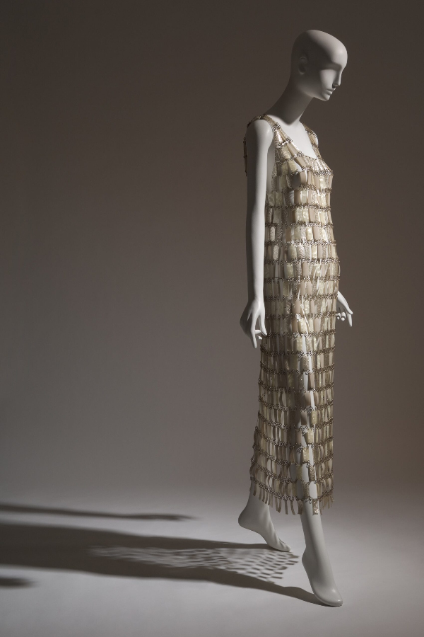 Ankle-length, sleeveless, shift-silhouette wedding dress made of white, pearlescent, and silver glitter plastic rectangles attached with metal loops in “chainmail” style.