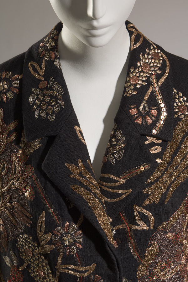 Close up view of black linen evening coat with large floral and vine embroidery made of metallic gold thread, metallic sequins, metal beading.