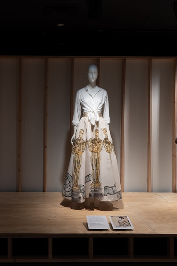 Floor-length A-line white cotton organdy skirt with hand-painted Oscar statuette motifs and curling film motifs around hem. Top of skirt is gathered and attached to a white satin waistband.