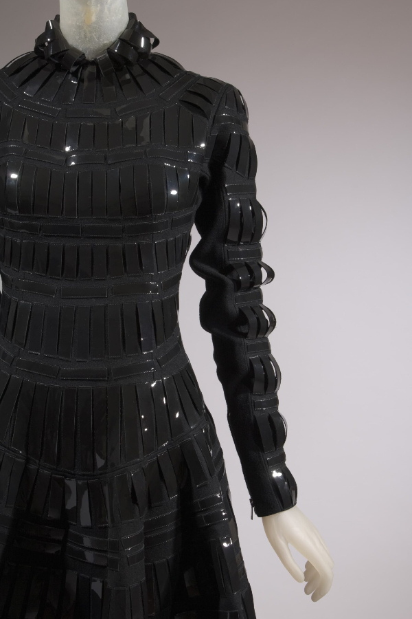 High neckline, long sleeve, full skirt black wool dress. Dress has vertical strips of patent leather from neckline to hem and from shoulder to wrist.