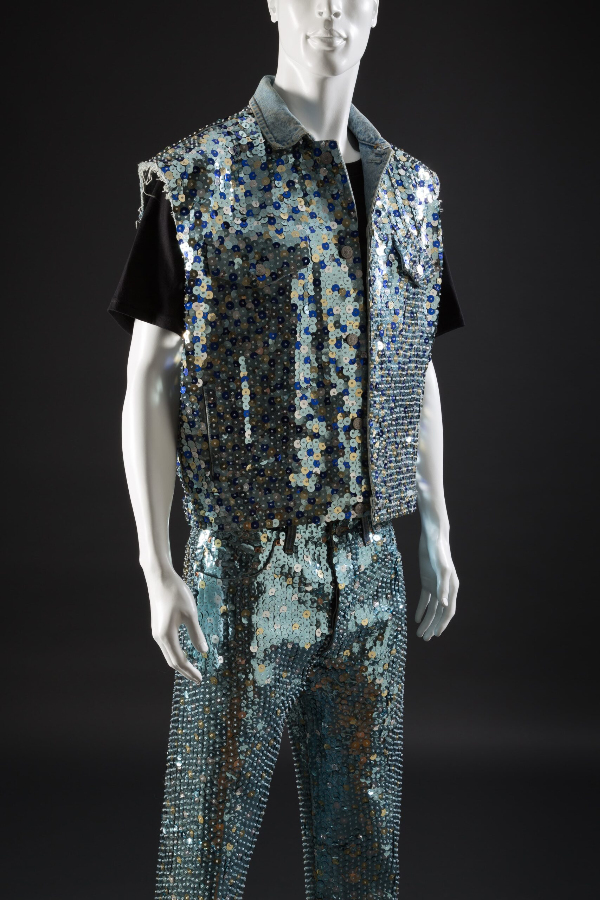 Man’s ensemble of denim vest and jeans covered in sequins in various shades of blue and gold.