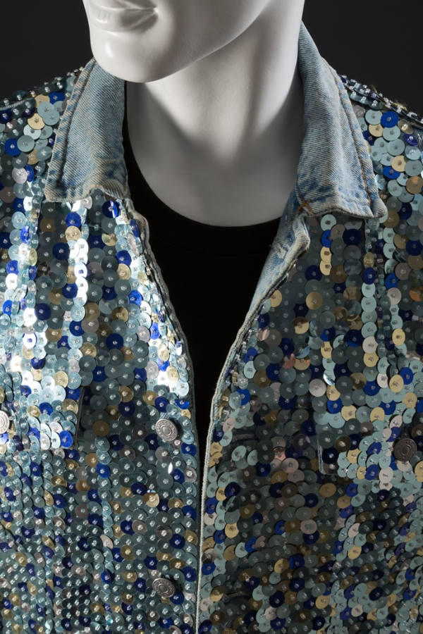 Man’s ensemble of denim vest and jeans covered in sequins in various shades of blue and gold.