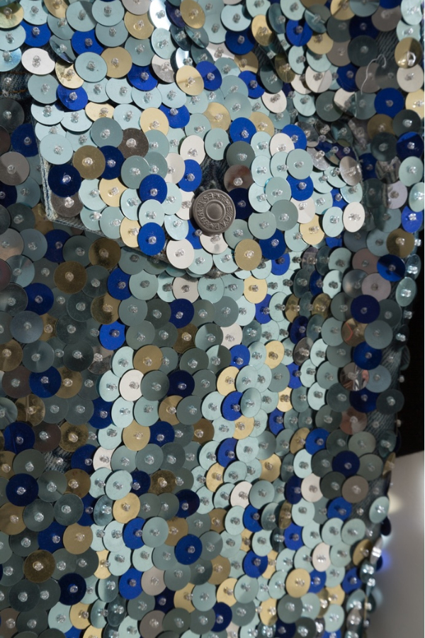 Man’s ensemble of denim vest and jeans covered in sequins in various shades of blue and gold.