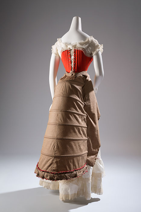 The bustle evolved from the crinoline during the late 1860s. It took many forms over the next twenty years, but all bustles were designed to emphasize the posterior. The more extreme bustle styles, such as those from the early 1880s, were often more elaborately structured. This example—a hybrid of a bustle and a petticoat—was sometimes referred to as a “crinolette.” Corset: Red wool, silk, steel, whalebone, circa 1880, possibly France, 98.29.3, museum purchase Bustle: Polka dot printed cotton, steel, circa 1880, USA, P83.29.1, museum purchase