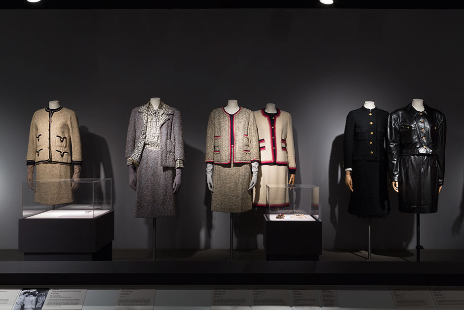 From left: Matlick Zelinka licensed copy of a Chanel suit, wool tweed, silk, braid, 1960, France, 71.245.1, gift of David Zelinka Jean-Louis Scherrer three-piece suit, wool tweed, silk, metal, circa 1964, France, 2014.15.24, gift of Cristina Noble Gabrielle “Coco” Chanel three-piece suit, wool and metallic tweed, 1963-1964, France, 80.13.1, gift of Ms. Georges Gudefin Adolfo three-piece suit, wool bouclé knit, silk, 1972, USA, 93.82.9, gift of Adolfo Gabrielle “Coco” Chanel suit, wool knit, cotton, metal, 1970, France, 87.139.7, gift of Mrs. Walter Eytan Karl Davis rain suit, embossed vinyl, brass, fall 1986, USA, 89.148.1, gift of Mr. & Mrs. Lembert Davis