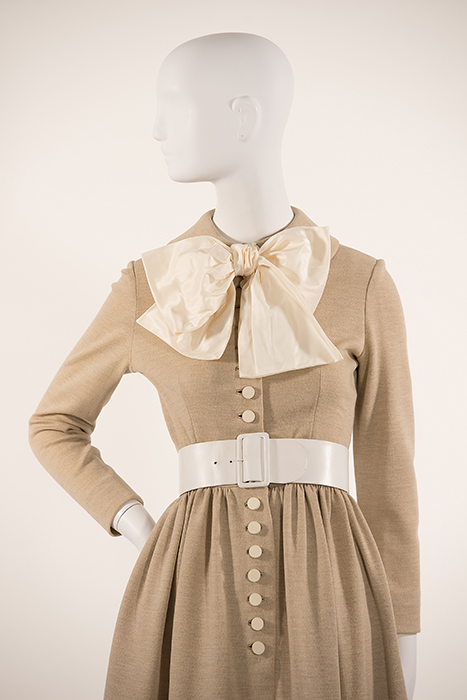 oatmeal colored dress with ivory buttons down center, white belt around waist and ivory bow at neck