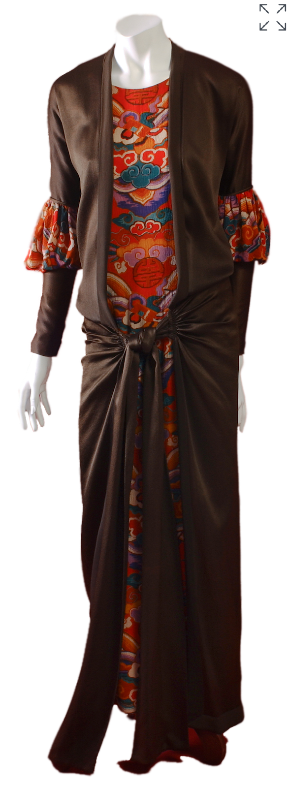 Front view of a 1927 Milgrim evening dress composed of a multicolor long sleeveless sheath in printed silk crinkle crepe with a woven cloud motifs underneath a long brown satin overdress knotted at the hips