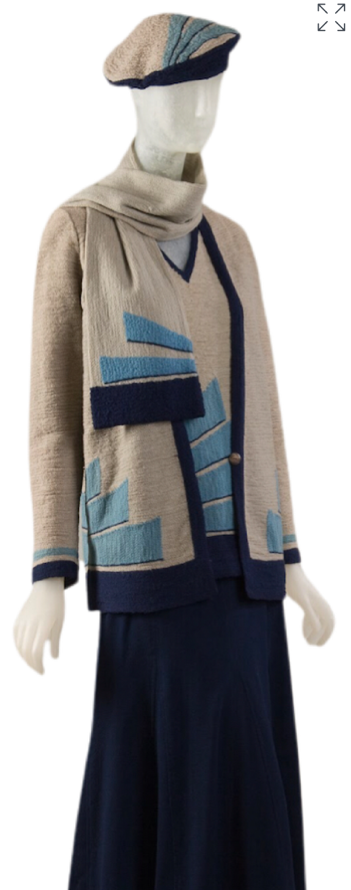 Front view of a 1929 ensemble by an unknown artist containing a hat, scarf, V neck top, and longsleeve cardigan made of the same grey wool knit fabric with a blue band at the edgs and turquoise rectangle motif. They are paired with a navy wool crepe skirt.