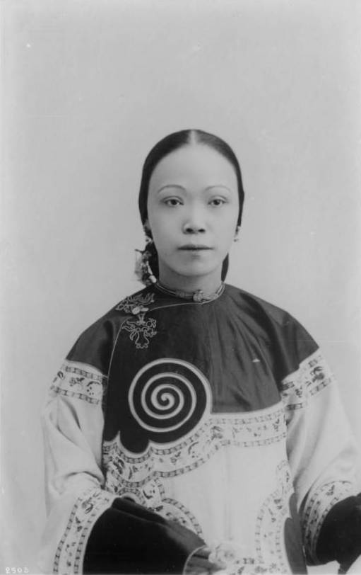 A young Chinese woman with her hair pulled back wearing a traditional Chinese blouse with a swirling design, circa 1920